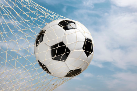 soccer ball in goal net against blue sky and white clouds backgroundの写真素材