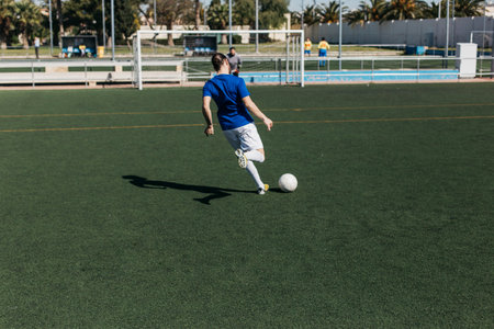 soccer player in blue uniform kicking ball on green field of stadium