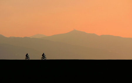 Silhouette of a cyclist at sunset, in the background the mountainsの写真素材