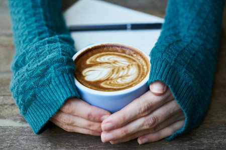Coffee cup with latte art in woman hands on wooden tableの写真素材