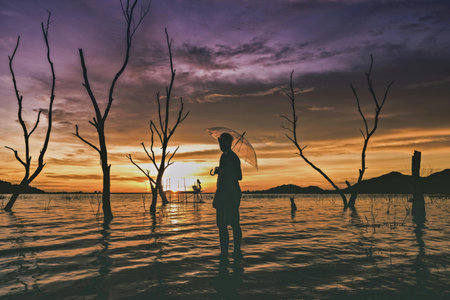 Silhouette of woman with umbrella in the sea at sunset.の写真素材