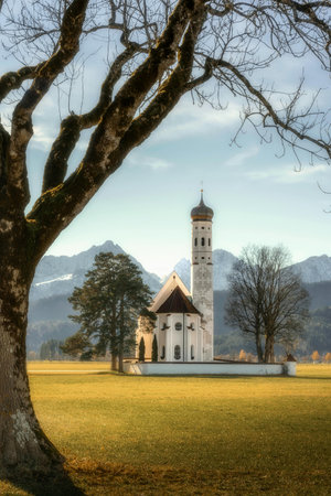 Church in a scenic landscape with a tower, surrounded by trees and grass, under a clear blue sky.の写真素材