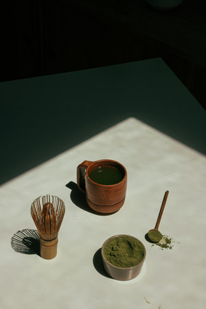 Matcha green tea powder in a clay cup and whisk on the table