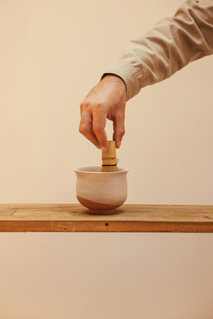 Hands holding mortar and pestle on wooden shelf against beige background