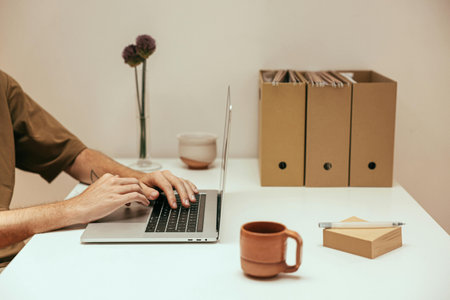 Cropped image of young man using laptop while sitting at desk in office