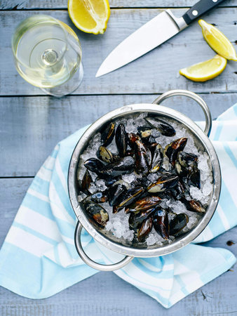 Mussels in ice bucket with lemon and white wine on wooden backgroundの写真素材