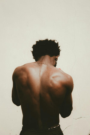 Back view of young man with muscular body standing against white wall.