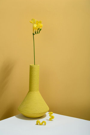 Yellow flower in vase on the table with yellow wall background.の写真素材