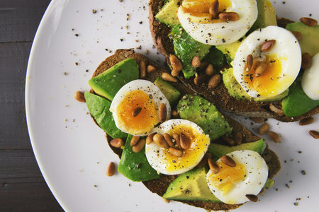Avocado toast with egg, sunflower seeds and pine nuts on white plate