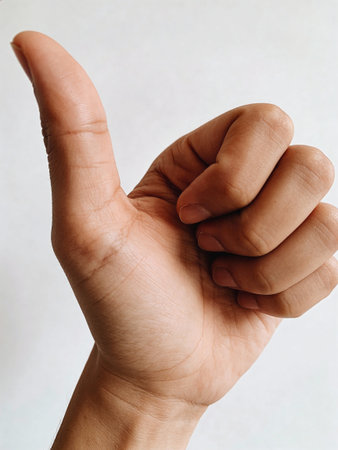 Hand showing thumbs up sign on white background. Close-up.