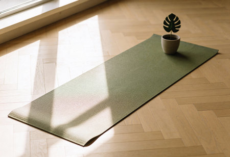 Green yoga mat with a plant on the floor in the room.