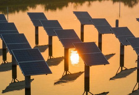 Solar panels in a row at sunset, with reflection in the waterの写真素材