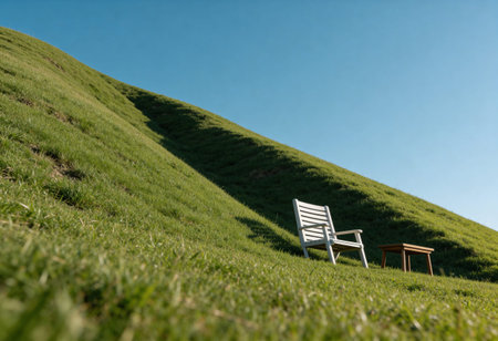 Wooden chair on grassy hillside against blue sky with copy spaceの写真素材