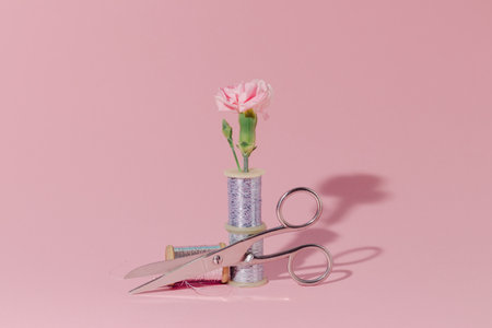 scissors, skein of thread and a bouquet of flowers on a pink background.の写真素材
