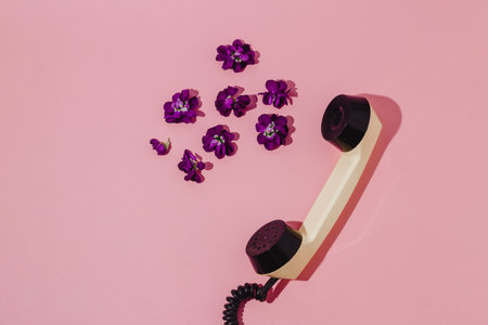 Retro telephone receiver with purple flowers on pink background. flat lay. organic technology.の写真素材