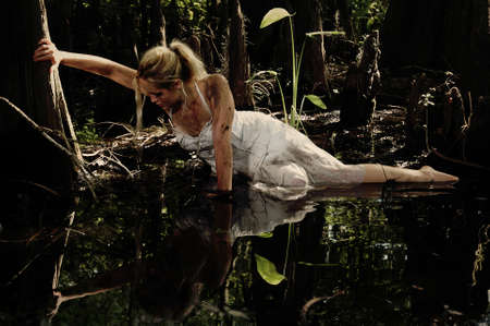 Girl grasping a tree trying to get out of a muddy bogの写真素材