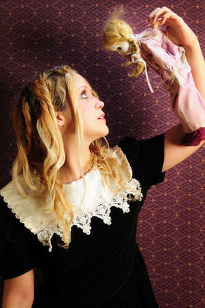 Doll-like girl in frilly dress holding porcelain doll up in front of herの写真素材