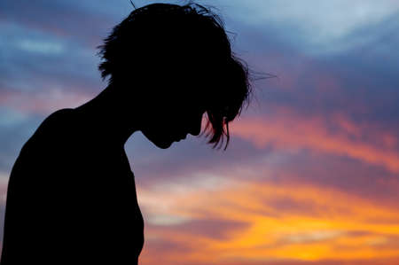 Female with head bowed in front of sunset skyの写真素材