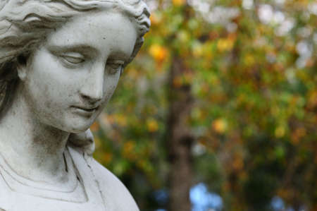 a female statue with a depressed look in front of a blurred out background of early fall leavesの写真素材