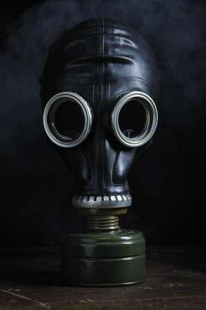 GGas mask sitting on an old wooden table top with smoky mist looming behindの写真素材