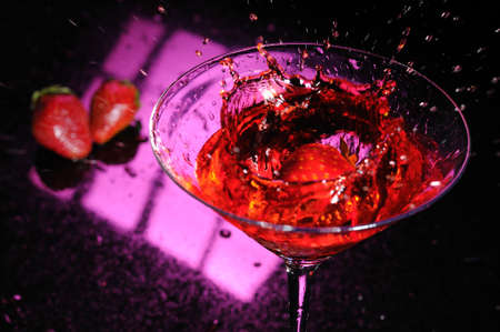 Strawberry splashing down in a martini glass filled with a red liquidの写真素材