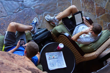 Orlando, FL USA. Aug 2012. Top view of two relaxed young men surfing and researching on phones and...