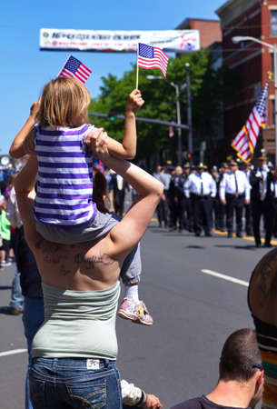 Middletown, CT USA. May 2018. Daughter sitting on mom`s shoulders waving flag during a Memorial Day celebration.のeditorial素材