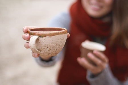 smiling girl holds two cups, one of which she hold out into the frame, autumn atmosphereの写真素材
