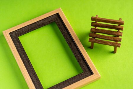 Miniature bench and empty frame against green background