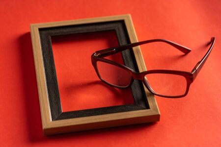 Spectacles and empty photo frame against red backgroundの写真素材