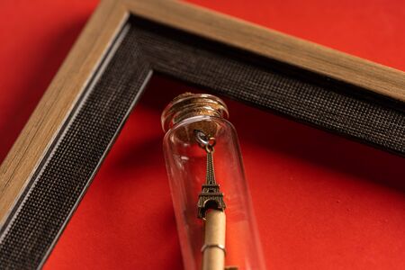 Miniature eiffel tower in bottle and empty frame against red background