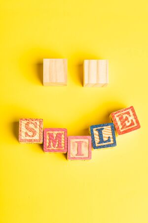 wooden blocks forming a smiling face against yellow background with Copy space for textの写真素材