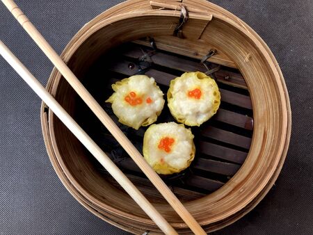Close up steaming Chicken Shumai (Shaomai, Siumaai) top with small fish eggs in bamboo steamer served as a dim sum snack for breakfast is delicious Chinese dumpling in traditional Cantonese cuisineの写真素材