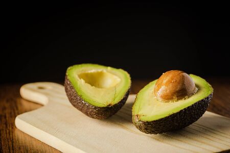 An avocado cut into half on a wooden cutting board with a dark backgroundの写真素材