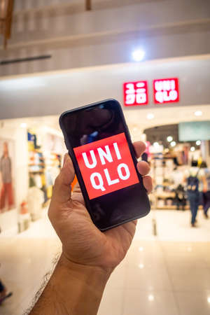 A man's hand holding an iphone X with uniqlo apps infront of Uniqlo store. Uniqlo apps is perfect for those who prefer online shoppingのeditorial素材