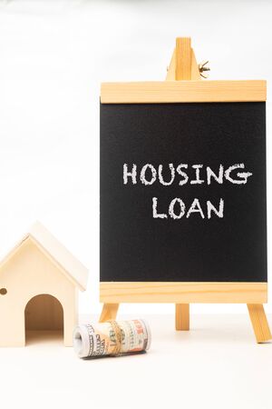 âHOUSING LOANâ wordings on a chalkboard with rolled up money and miniature houseの写真素材