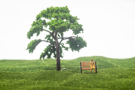 Miniature figure if an old man sitting on a bench under a treeの写真素材