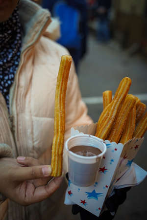 Closed up shot of a woman holding a churros with chocolate dippingsの写真素材