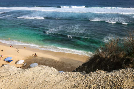A wide angle shot at Pandawa Beach, Bali with parasols on sandy beach with strong waves at the ocean...