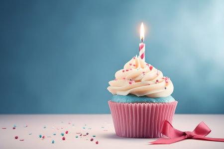 Birthday cupcake with burning candle and pink bow on blue backgroundの素材
