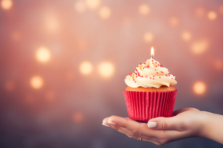 Birthday cupcake with candle in female hands on bokeh backgroundの素材