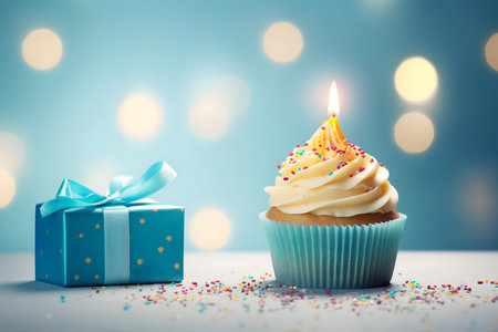 Birthday cupcake with candle and gift box on blue bokeh backgroundの素材