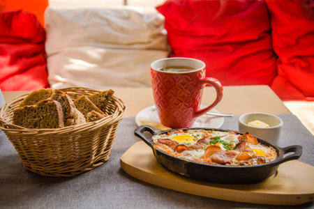 Light-filled Polish restaurant serving polish breakfast Ham, Gouda cheese, egg, tomato, cucumber, cream cheese, butter with a basket of bread and a cup of coffeeの写真素材
