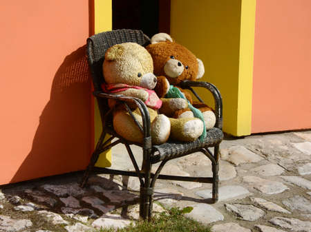 Two big teddy bears sitting on a wooden chair in front of a houseの写真素材