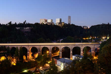 Old railway viaduct in Luxembourg with a train light line, modern buildings in backgroundの写真素材