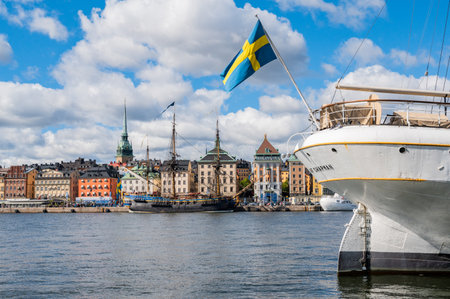 Old ship with a flag of Sweden in foreground, with another big sailing ship anchored in Stockholmの写真素材
