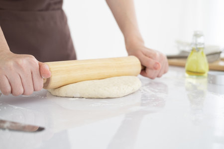 Woman in apron rolling dough on white table in bright clean kitchen with wooden rolling pin. Close up. Copy Spaceの写真素材