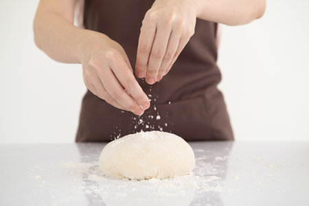 Woman sprinkling flour over fresh dough on white bright kitchen table.の写真素材