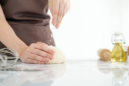 Cook hands kneading dough, sprinkling piece of dough with white wheat flour. Low key shot, close up on hands, some ingredients around on table.の写真素材