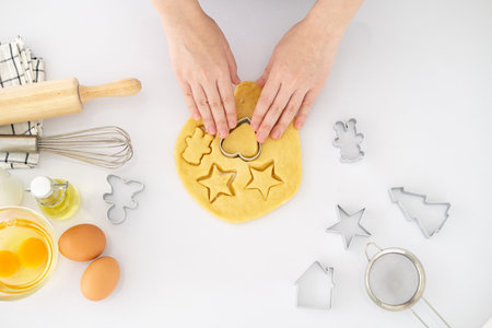 Cropped image of hands cutting cookies of dough while baking in kitchen .Making for homemade biscuits. On the table is dough and a set of cookie molds with other kitchen equipment.の写真素材